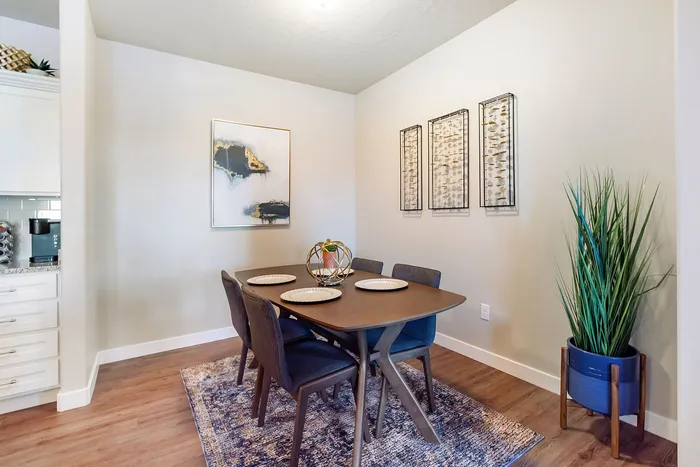 Chic dining area with elegant table setup, modern art pieces, and a lush plant accent on warm wood flooring.