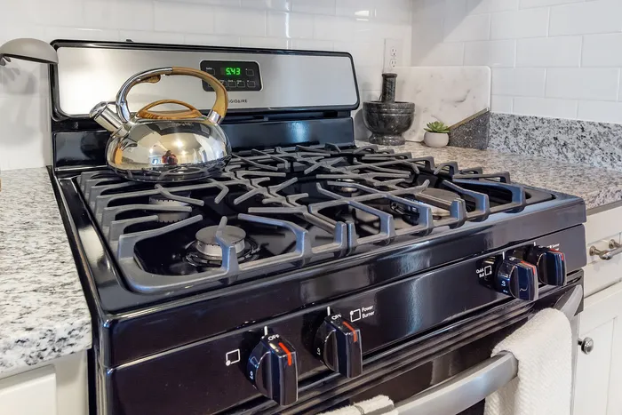 Modern kitchen with polished black stove and elegant kettle on granite countertop.