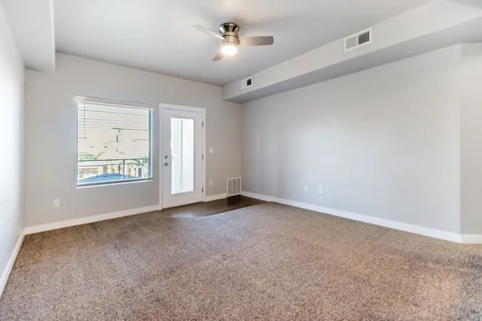 Bright living space with large window, plush carpet, and modern ceiling fan offering a welcoming atmosphere.