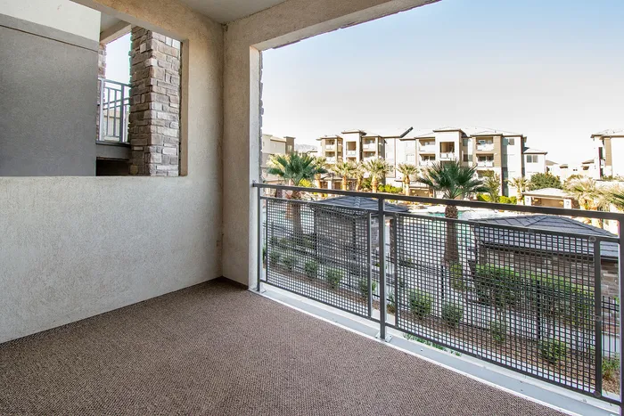 Charming apartment balcony with stone accents, overlooking a lush courtyard with palm trees and modern apartment buildings.
