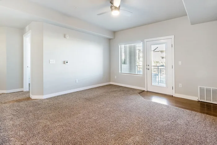 Bright and spacious room with plush carpet, modern ceiling fan, and access to a private balcony through glass doors.