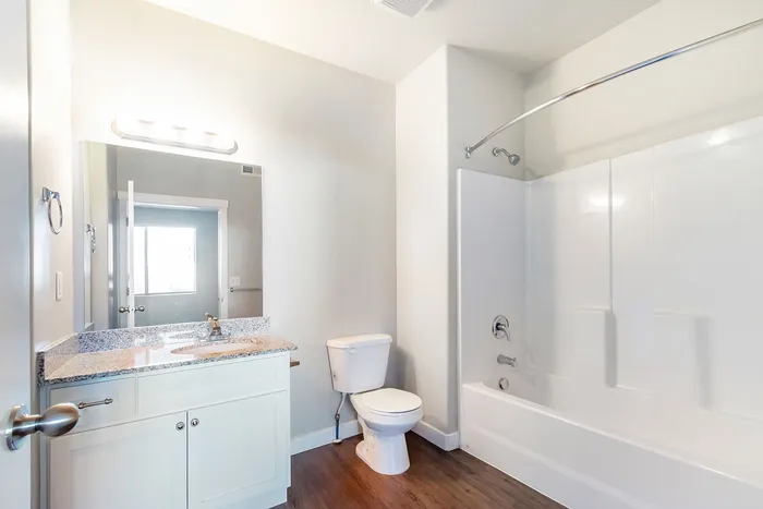 Bright bathroom featuring sleek white cabinetry, a granite countertop, and a modern tub-shower combo with elegant chrome fixtures.
