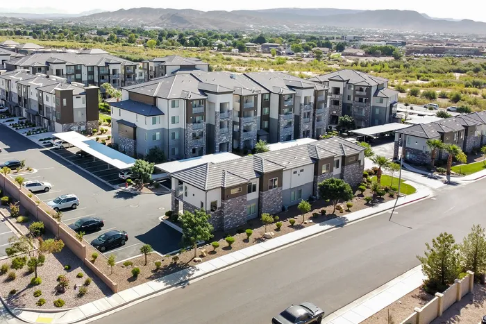Modern apartment complex with stylish architecture surrounded by picturesque landscapes, featuring ample parking and lush greenery.