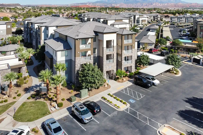 Modern apartment complex featuring landscaped gardens, multiple levels, and ample parking, surrounded by stunning mountain views.