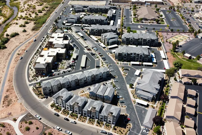 Aerial view of a modern apartment complex, showcasing a well-planned urban layout with lush green areas and ample parking.