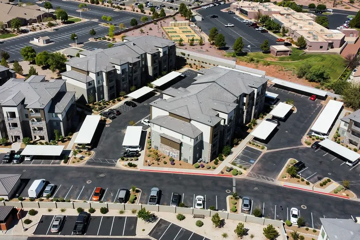 Modern apartment complex aerial view with landscaped grounds, spacious parking, and nearby recreational courts.