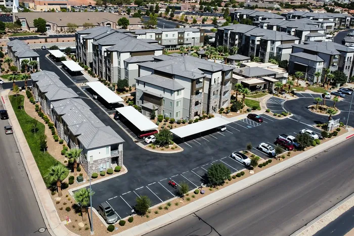 Aerial view of a modern apartment complex featuring stylish architecture, lush landscaping, and ample parking spaces, offering an ideal living environment.