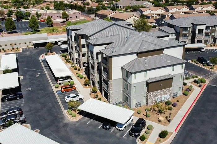 Aerial view of modern apartment complex with well-maintained landscaping and ample parking spaces under covered carports.