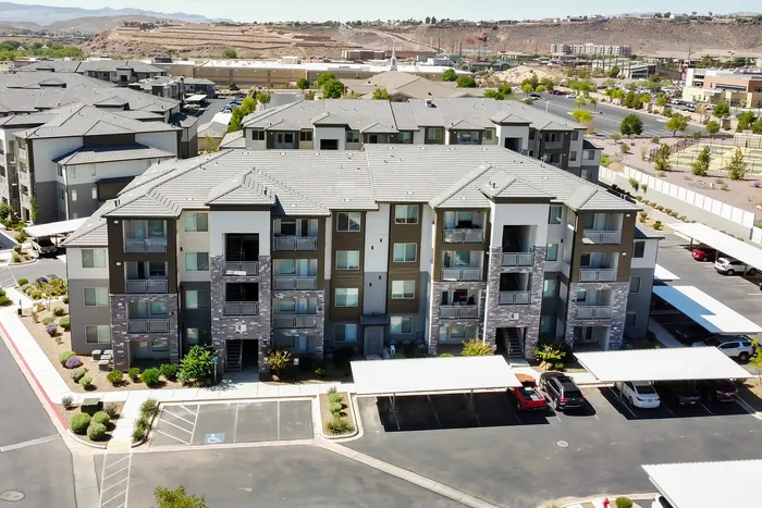 Modern apartment complex featuring well-maintained landscaping, multiple stories, and ample parking, set against a scenic hillside backdrop.