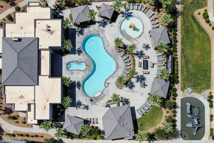 Aerial view of a luxurious apartment complex featuring a uniquely shaped swimming pool, relaxing lounging areas, and lush landscaping.