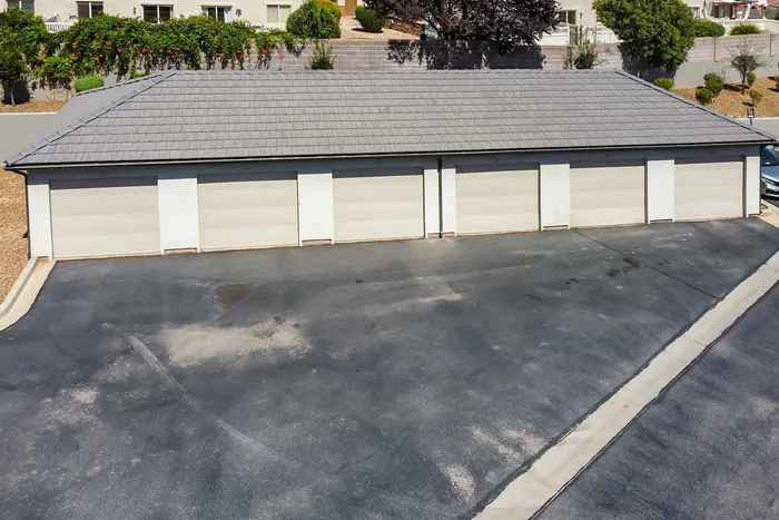 Charming row of garage units with a neatly paved driveway and lush greenery backdrop, offering ample parking and storage solutions.