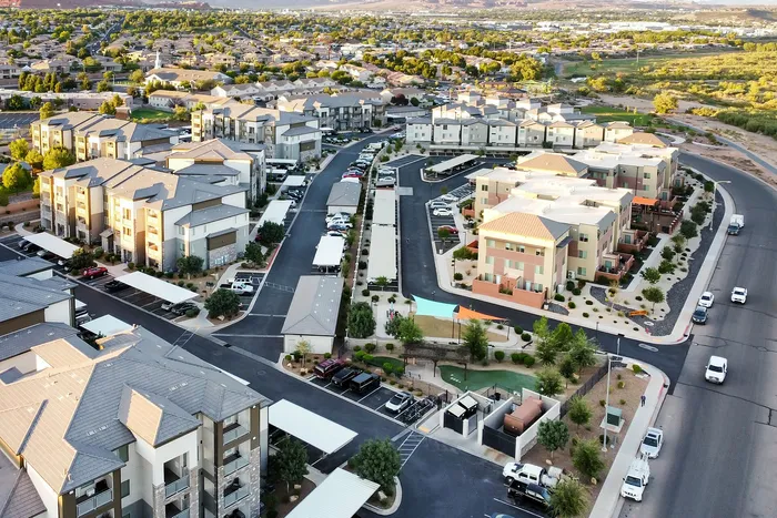 Aerial view of modern apartment complex with landscaped gardens, ample parking, and scenic surroundings, perfect for comfortable living.