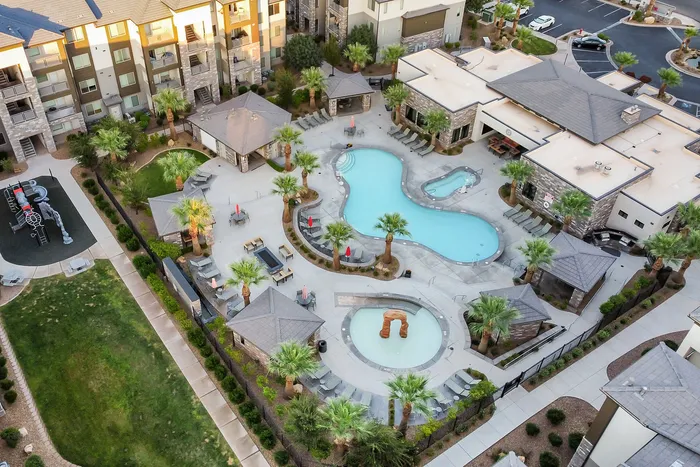 Aerial view of a luxurious apartment complex with a resort-style pool, palm trees, and cozy cabanas, offering a tropical oasis atmosphere.