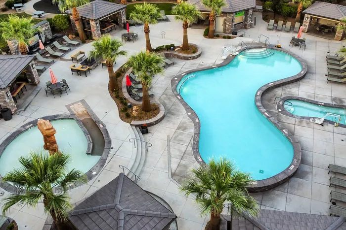 Luxurious resort-style apartment complex with a stunning freeform pool, surrounded by lush palm trees and elegant outdoor seating areas.