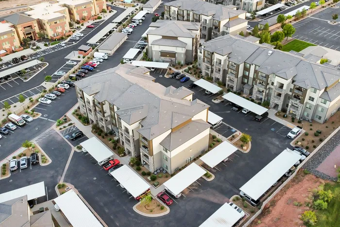 Aerial view of a modern apartment complex featuring well-maintained buildings, ample parking spaces, and lush landscaping.