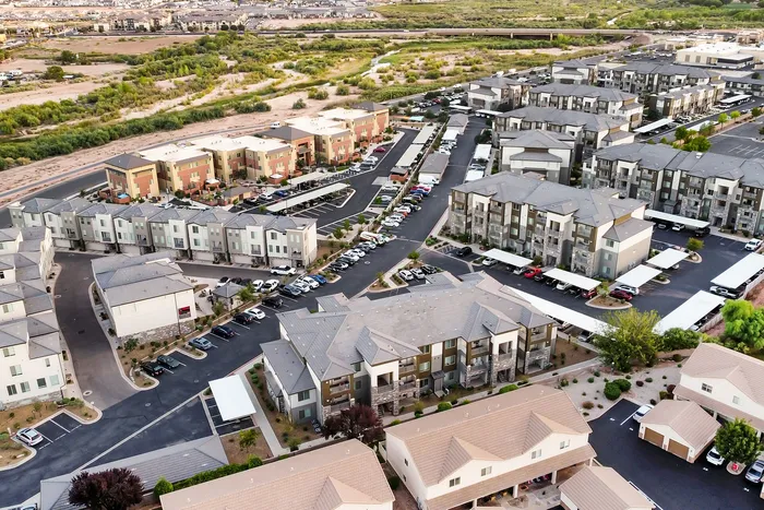 Aerial view of a modern apartment complex surrounded by lush green landscapes, ample parking, and well-maintained pathways.
