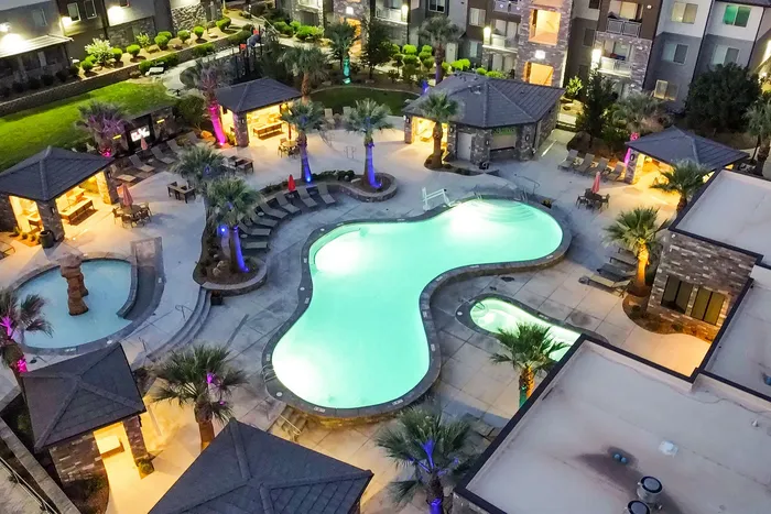 Luxurious apartment complex with a sparkling resort-style pool, elegant cabanas, and vibrant evening lighting.