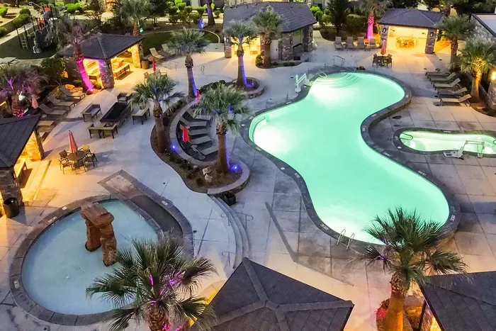 Luxurious resort-style pool area with palm trees, ambient lighting, and cozy lounge spaces for relaxation.