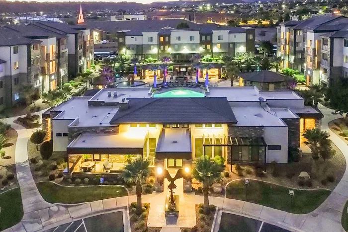 Stunning aerial view of a modern apartment complex at dusk, featuring a central illuminated pool, vibrant landscaping, and elegant architecture.