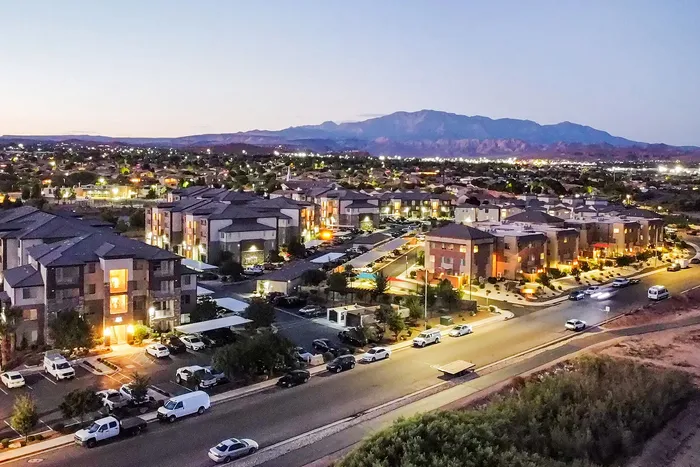 Charming apartment complex at dusk with illuminated buildings and mountain views, offering a serene and picturesque residential setting.