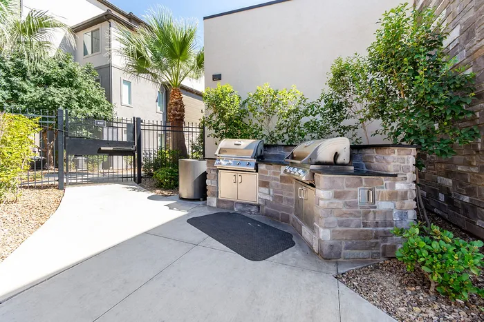 Inviting outdoor patio with stone grill area, lush greenery, and modern amenities for perfect alfresco dining.