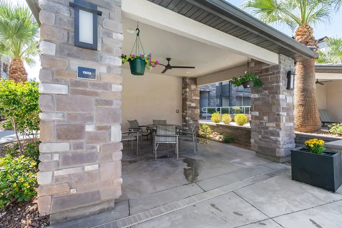 Charming outdoor patio with modern stone pillars, lush greenery, and vibrant hanging plants, perfect for relaxation.