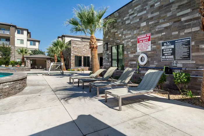 Luxurious apartment complex with a stylish stone exterior, featuring a relaxing swimming pool area surrounded by palm trees and comfortable lounge chairs.
