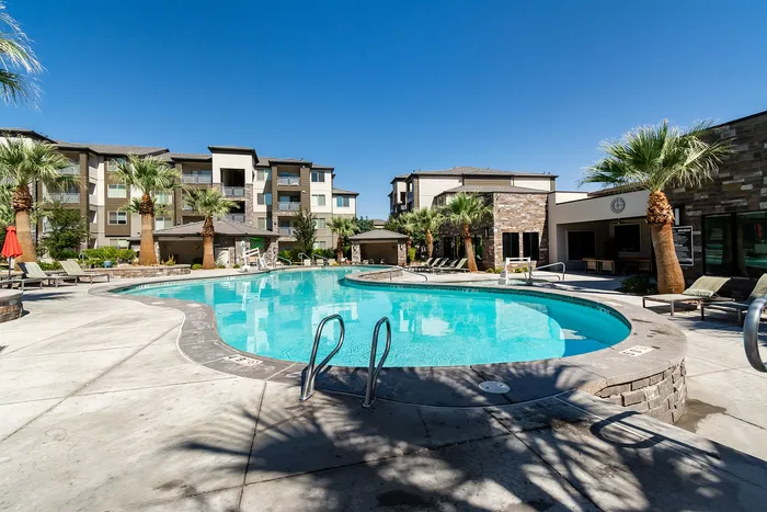 Luxurious apartment complex featuring a sparkling pool, surrounded by lush palm trees and modern architecture under a clear blue sky.