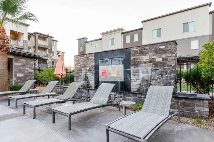 Modern apartment complex with cozy lounge area, featuring stylish reclining chairs and elegant stone water feature, perfect for relaxation and leisure.