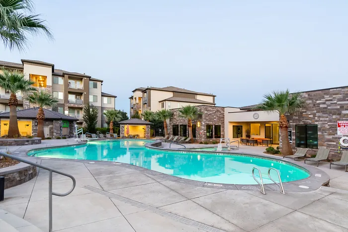 Luxurious apartment complex with a sparkling outdoor pool, modern amenities, and palm tree landscaping under a serene sky.