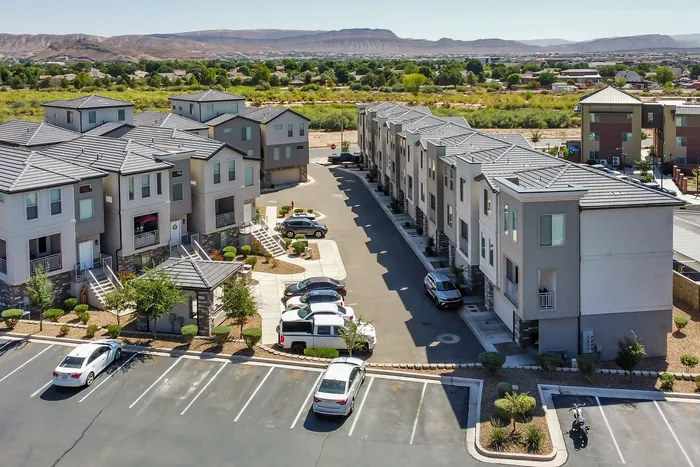 Modern apartment complex with stylish gray buildings, lush landscaping, and ample parking, set against a scenic mountain backdrop.