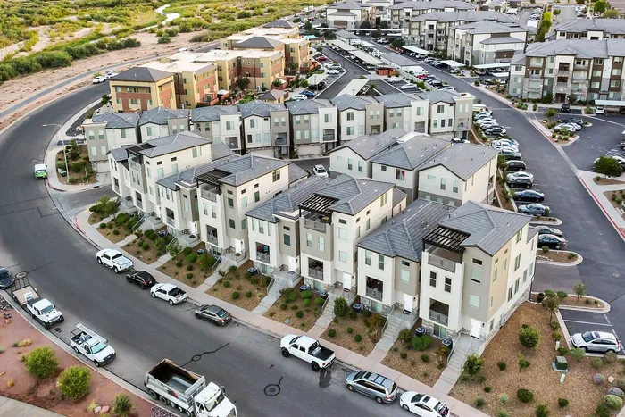 Aerial view of a modern apartment complex with a row of stylish townhouses, ample parking, and lush green surroundings.