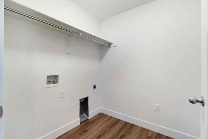 Bright and spacious laundry room with sleek white walls and warm wooden flooring, ready for washer and dryer installation.