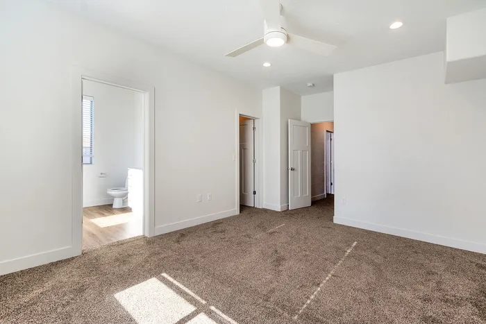 Bright and spacious bedroom with plush carpeting, ceiling fan, and an ensuite bathroom featuring modern fixtures.