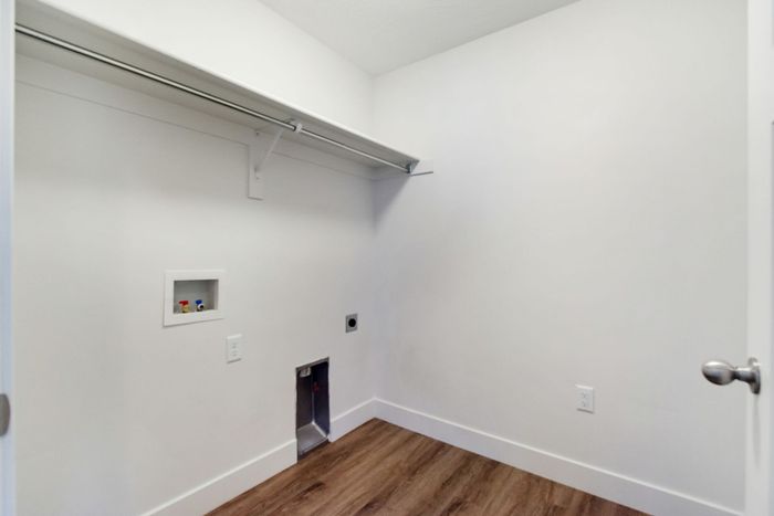 Spacious laundry room with sleek white walls and modern wood flooring, ready for appliances.