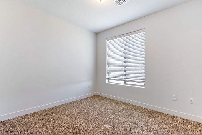 Bright and cozy room with soft carpet flooring and a large window with blinds.