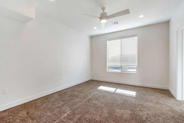 Bright and airy bedroom featuring plush carpeting, a ceiling fan, and ample natural light from large windows.
