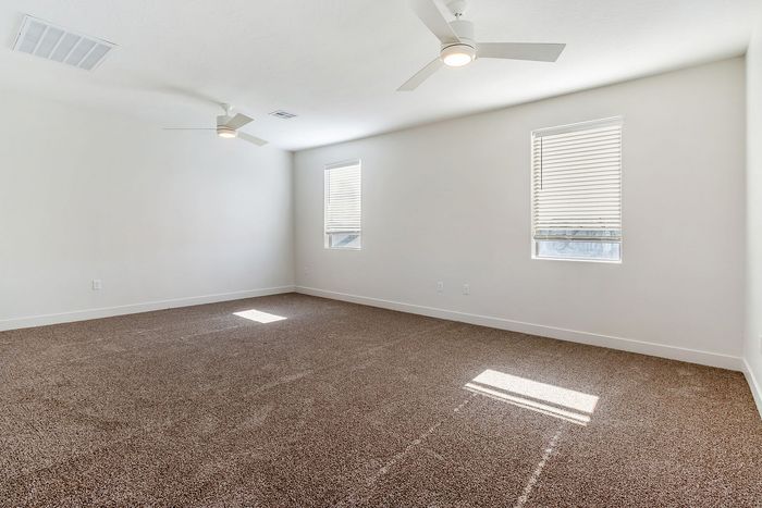 Spacious, sunlit room with plush carpeting and modern ceiling fans, perfect for a cozy bedroom or a versatile living space.