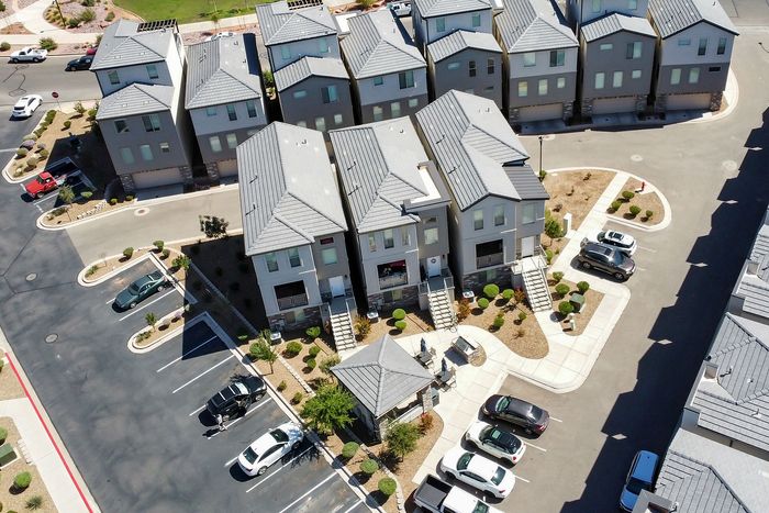 Aerial view of a modern residential complex featuring multiple three-story townhouses with stylish rooftops, ample parking, and landscaped surroundings in a serene neighborhood setting.