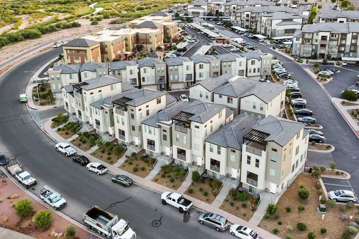 Aerial view of modern townhomes in a vibrant community with sleek architecture and ample parking, surrounded by lush greenery and scenic pathways.