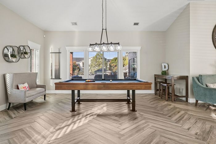 Apartments in Ogden, UT, with In-Unit Washer and Dryer - Pinebrook Apartments - Game Room With Pool Table, Lounge Seating, Large Windows, Herringbone Flooring, And Modern Globe Chandelier.