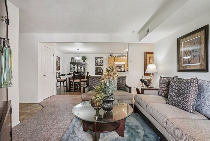 Elegant living room with cozy seating, a stylish glass coffee table, and a view into a chic dining area, featuring modern decor and warm lighting.