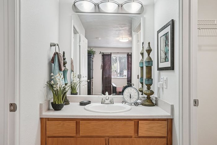 Elegant bathroom vanity with wooden cabinets, chic decor, and a large mirror reflecting natural light from a nearby room.