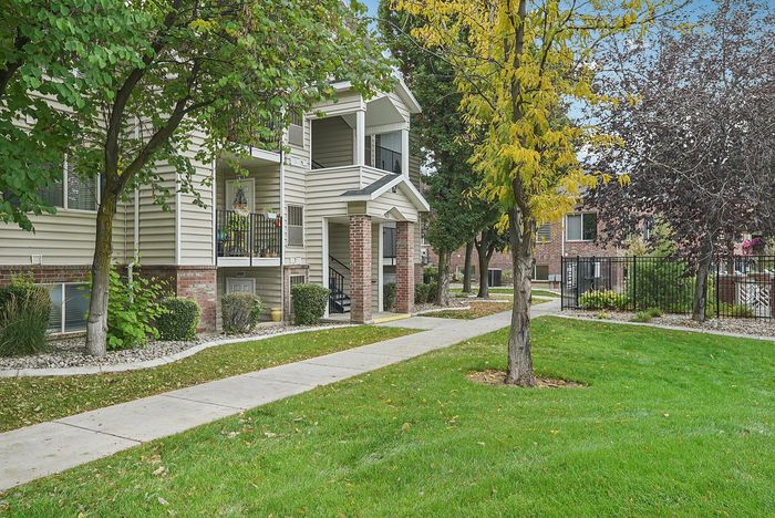 Charming apartment exterior with a lush green lawn, mature trees, and a welcoming balcony, perfect for enjoying outdoor relaxation.