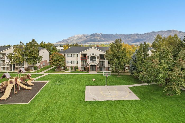 Charming apartment complex with scenic mountain views, lush green lawns, a playground, and basketball court nestled amid mature trees.
