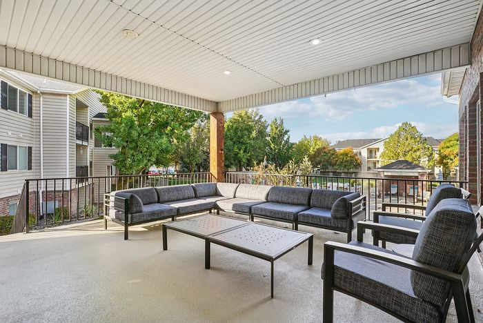 Inviting covered patio with modern outdoor seating overlooking a peaceful apartment complex and lush green surroundings.