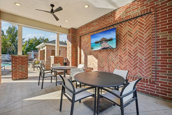 Charming outdoor patio with modern brick accents, ceiling fan, and poolside view, perfect for relaxing and entertaining.