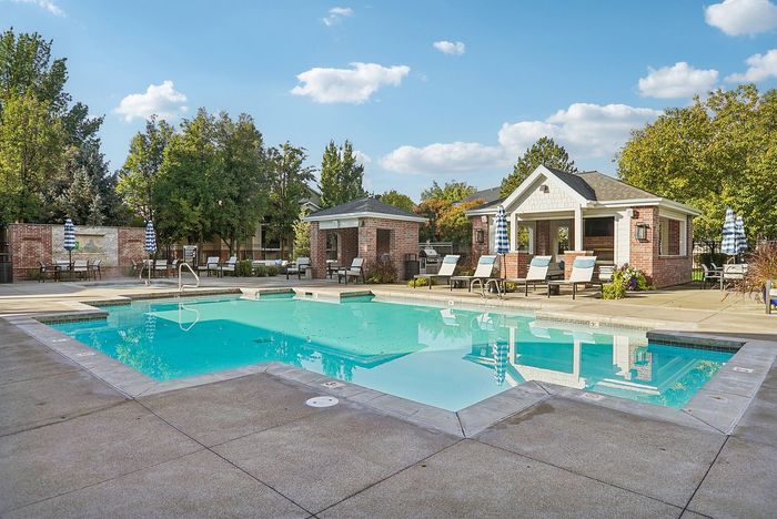 Inviting outdoor pool with elegant lounge chairs, surrounded by lush trees and charming brick architecture, perfect for relaxation.