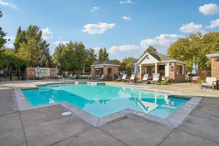 Inviting community pool area surrounded by lush trees and cozy lounging chairs, perfect for relaxation and leisure.