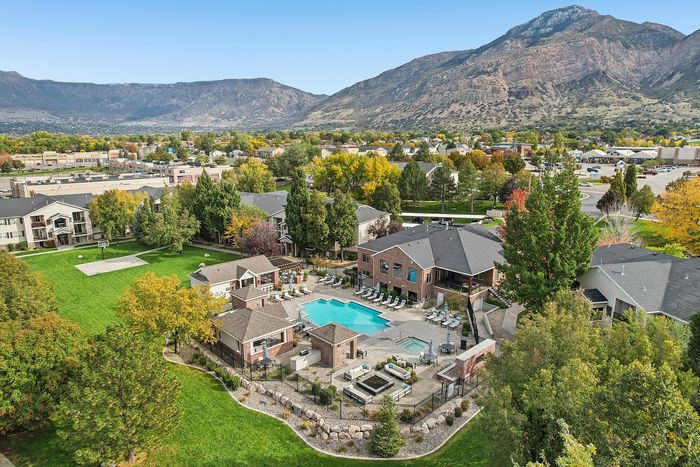Scenic aerial view of a vibrant apartment complex with a sparkling pool, lush green landscaping, and majestic mountain backdrop, offering a perfect blend of relaxation and outdoor beauty.